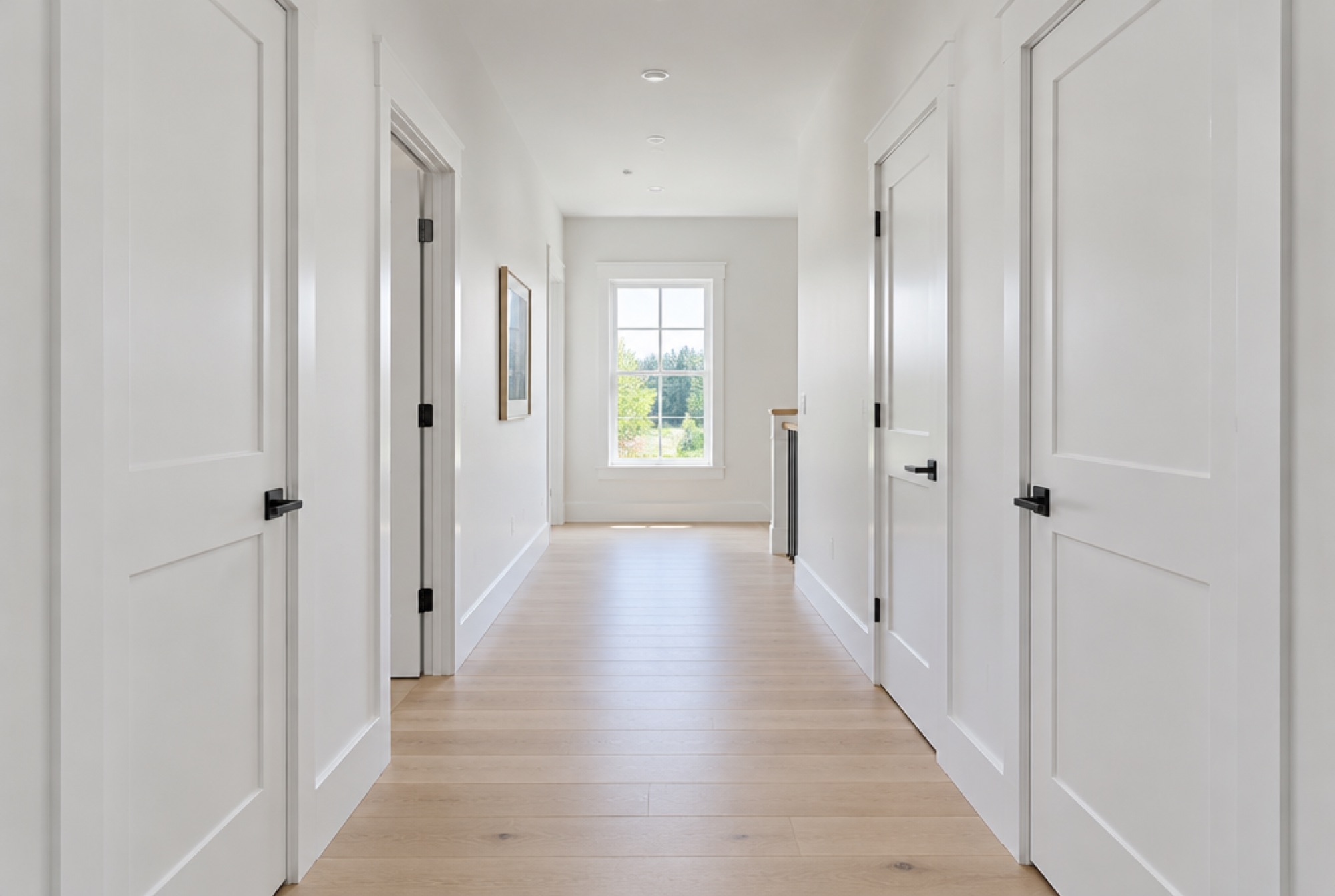Bright hallway with white Shaker interior doors, black levers, crisp casings and tall baseboards